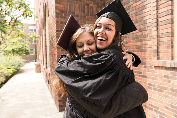 Happy American Mother Hugs Daughter Celebrating Graduation Day USA This is a horizontal, color photograph of a beautiful, young Millennial woman wearing a graduation hat as she hugs her mother during the celebration for the commencement graduation from college. Photographed with a Nikon D800 DSLR camera. puerto rican ethnicity stock pictures, royalty-free photos & images