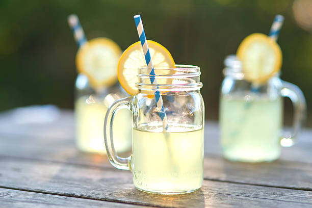 Lemonade glass jars with lemon wedges and straws Lemonade glass jars with lemon wedges and straws sitting on a wood tabletop lemonade stock pictures, royalty-free photos & images