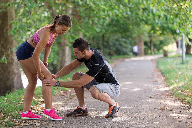 l'uomo aiuta la donna con il ginocchio infortunato all'attività sportiva - human knee physical injury bandage muscular build foto e immagini stock