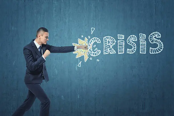 Photo of Businessman punching hard the word 'crisis' written on dark blue