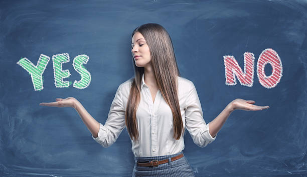 Beautiful businesswoman standing with open palms between big colorful words A beautiful businesswoman standing with open palms between the big colorful words 'yes' and 'no' written on the dark blue background. Decision-making under uncertainty and risk conditions. A hard choice to make. Solving business problems. single word no stock pictures, royalty-free photos & images