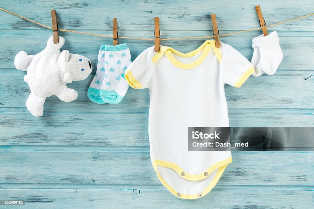 Baby clothes, onesie, socks, white bear toy on a clothesline Baby boy clothes, onesie with socks and white bear toy on a clothesline Baby - Human Age Stock Photo