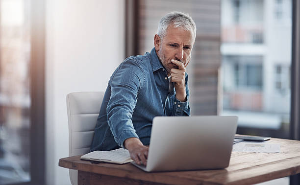 Working through ways to better manage his business Cropped shot of a thoughtful mature businessman working on a laptop in an office mature businessman stock pictures, royalty-free photos & images