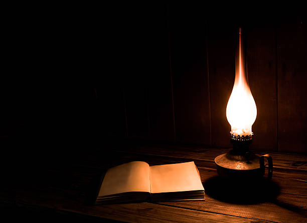 Old book with burning paraffin lamp on the wooden table.