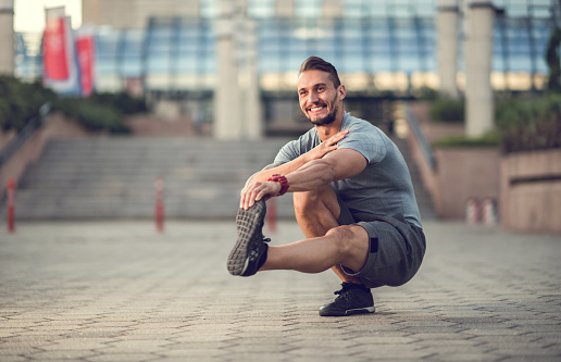 Happy sportsman standing on one leg in a squat while stretching his other leg.