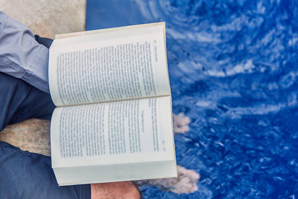 istock Adult man reading book while sitting in poolside 622921900