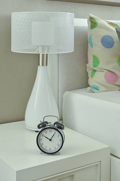 istock Clock and white lamp on bedside table in bedroom 622955556