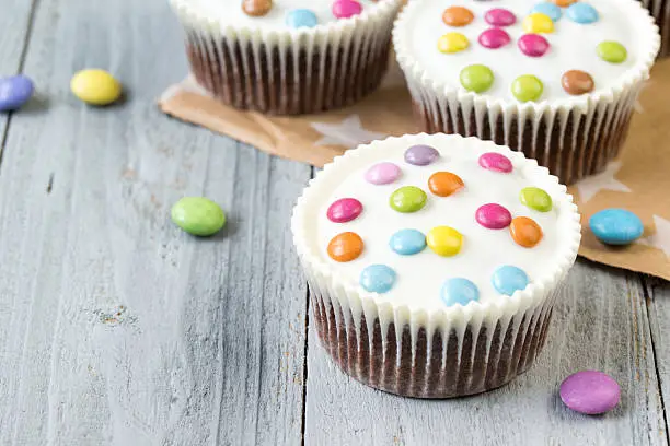 Chocolate cupcakes with white icing and colored smarties, wooden background