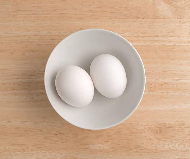 dois ovos em uma tigela em cima de uma mesa de madeira. - two eggs - fotografias e filmes do acervo