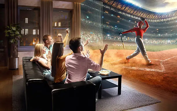 :biggrin:A group of young friends are cheering while watching extremely realistic Soccer game at home. They are sitting on a sofa in the modern living room faced to a real stadium with players instead of the front wall. It is evening outside the window.