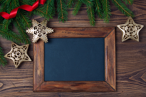 Merry Christmas decorations, empty chalkboard and frame made of red ribbon, fir, snowflake and stars on a timber background