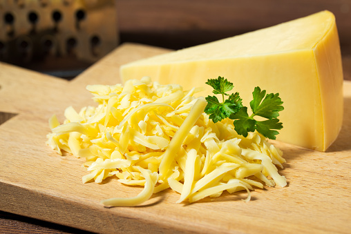 Grated cheese and cheese triangle on wooden cutting board, close up