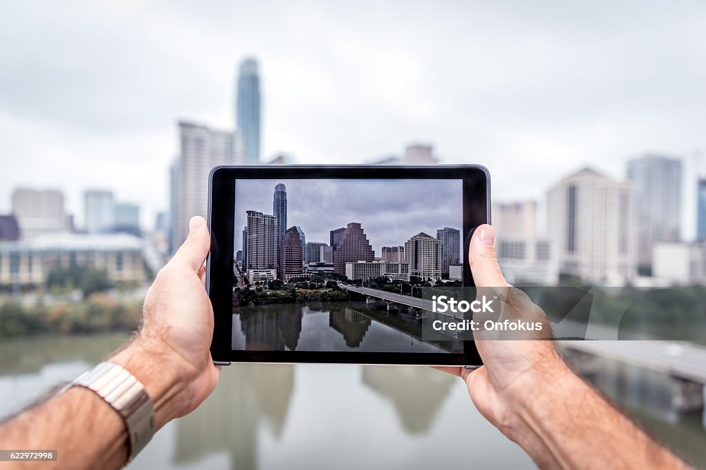 Human Hands Holding a Digital Tablet in Austin Texas Human Hands Holding a Digital Tablet in Austin Texas. The city is visible on the tablet and also in the background. Internet Stock Photo