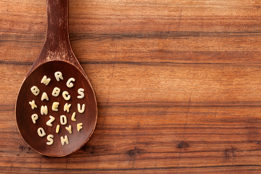 Top view of wooden spoon over table with alphabet soup letters on it