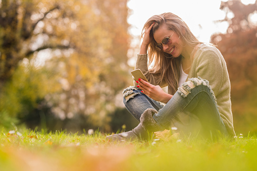 Smiling young woman is using phone and enjoying in nature