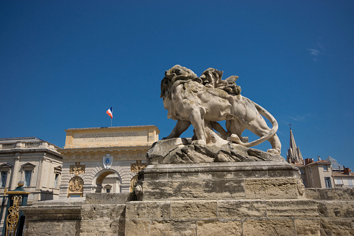 Montpellier, France - August 5, 2015: Palais de Justice in Montpellier under a clear polarized sky. In the foreground is a lion statue with the Arc de Triomphe in the background.