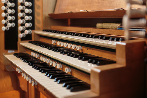 A traditional wooden church organ shot in shallow depth of field from the side showing keys and pull out stops.