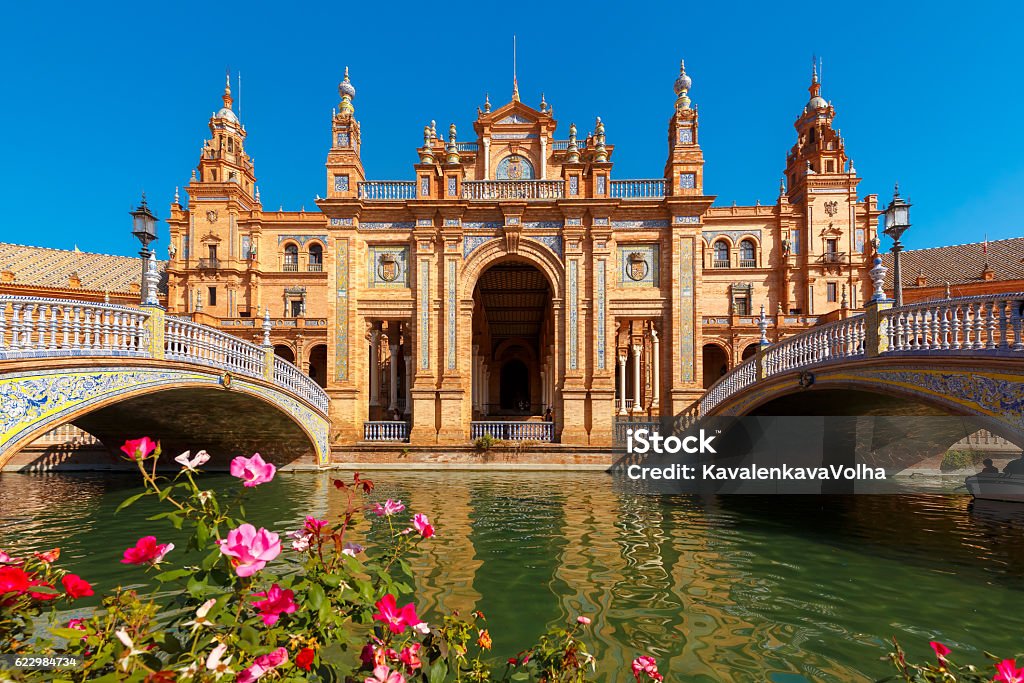 Plaza de Espana at sunny day in Seville, Spain Spain Square or Plaza de Espana in Seville in the sunny summer day, Andalusia, Spain. Flower beds, bridges and channel in the foreground Seville Stock Photo