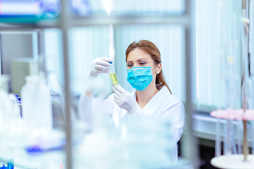 Woman in laboratory, examining new potions for the scientific research at university. Woman is wearing protective mask and protective gloves (Surgical gloves) while working with beakers, test tubes and other lab equipment. Series of images, taken with Nikon D800 and 50mm or 85 mm professional lens, developed from RAW.