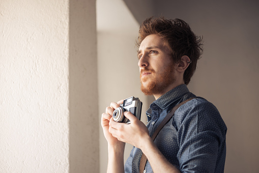 Hipster man searching for an interesting subject for his photo shooting and holding a vintage camera