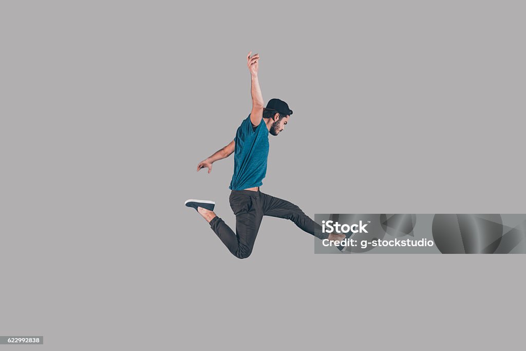 Like a rock star. Mid-air shot of handsome young man in cap jumping and gesturing against background Jumping Stock Photo