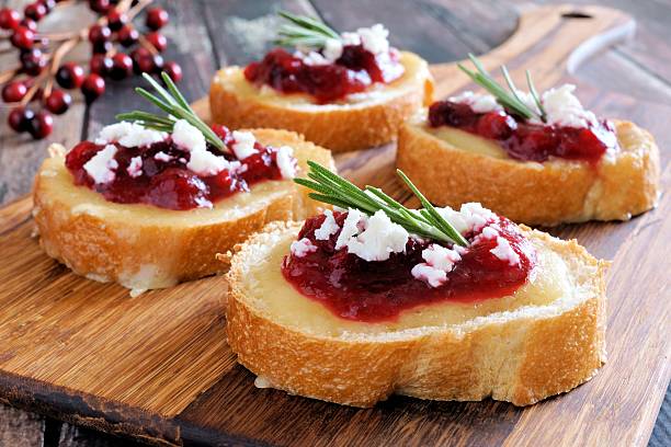 Crostini appetizers with cranberry sauce, cheese, rosemary on wooden server Holiday crostini appetizers with cranberry sauce, brie, feta and rosemary on a wooden server brie stock pictures, royalty-free photos & images