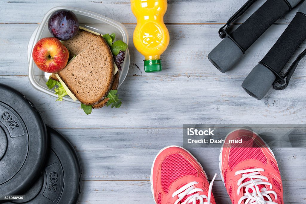 Fitness concept, pink sneakers, weight plates, dumbbells, sandwich Fitness concept, pink sneakers, weight plates, dumbbells, sandwich, fruits and orange juice, wooden background, top view Health Club Stock Photo