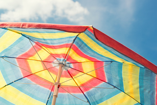 Colorful beach umbrella yellow, red, blue against blue sky, vintage filter