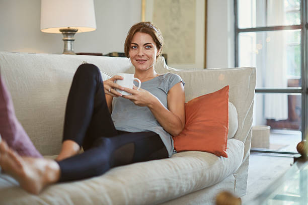Woman lying down on the sofa and enjoying tea. Woman lying down on the sofa and enjoying tea. Lifestyle shot in real location, Spain. yoga pants photos stock pictures, royalty-free photos & images