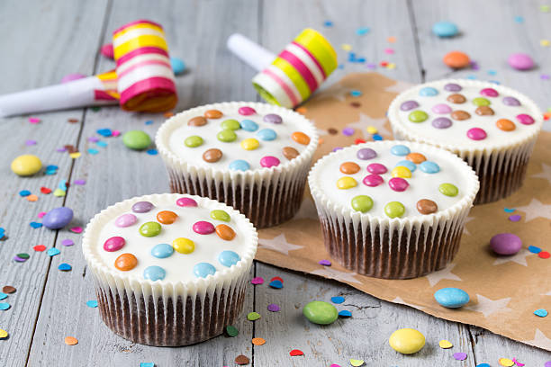 istock Cupcakes with white icing and colored smarties, party horns 623104032