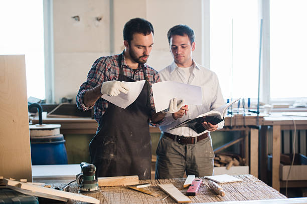 istock Happy male carpenter showing something to coworker at his notebook 623111384