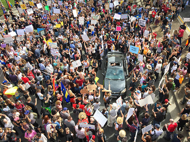 Los Angeles, United States - November 12, 2016: Thousands of Angelenos marched through the streets of Downtown Los Angeles in protest of president-elect Donald Trump. A young woman in a vehicle stuck in the marching crowd stands out of the sunroof and honks the horn with chanting protesters.