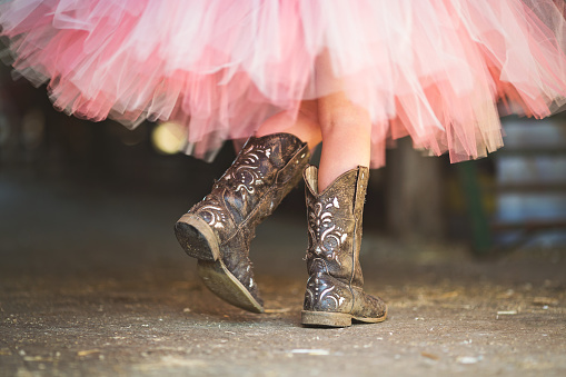 Princess Cowgirl. Little cowgirl walking though a barn in her boots and pink tutu in the afternoon sun.