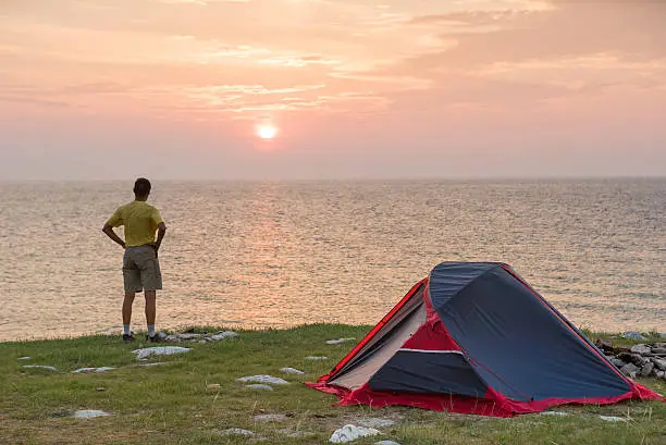 Sunrise in camping day. Alone tourist stands near tent and enjoy beautiful view.