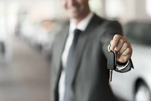 Smiling car salesman handing over your new car keys, dealership and sales concept