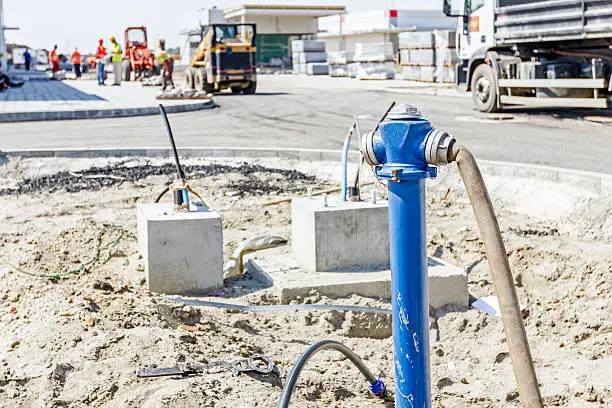 Water hose is attached to newly placed fire hydrant on construction site.
