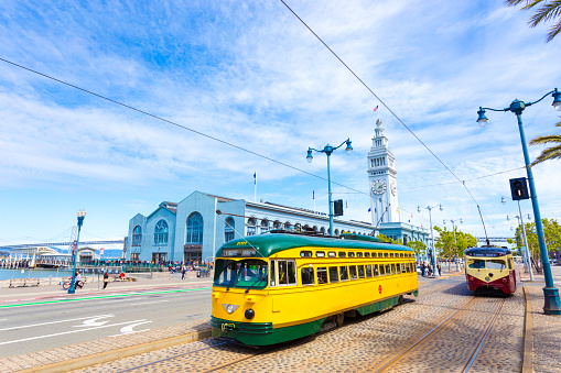 San Francisco, United States - May 23, 2016: Two vintage F market streetcars pass in front of Ferry Building on Embarcadero and Bay Bridge in background on a sunny, blue sky day