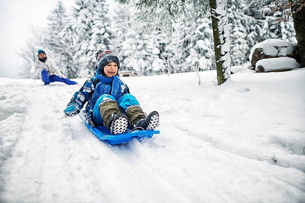 madre e figlio che giocano nella neve - sled foto e immagini stock