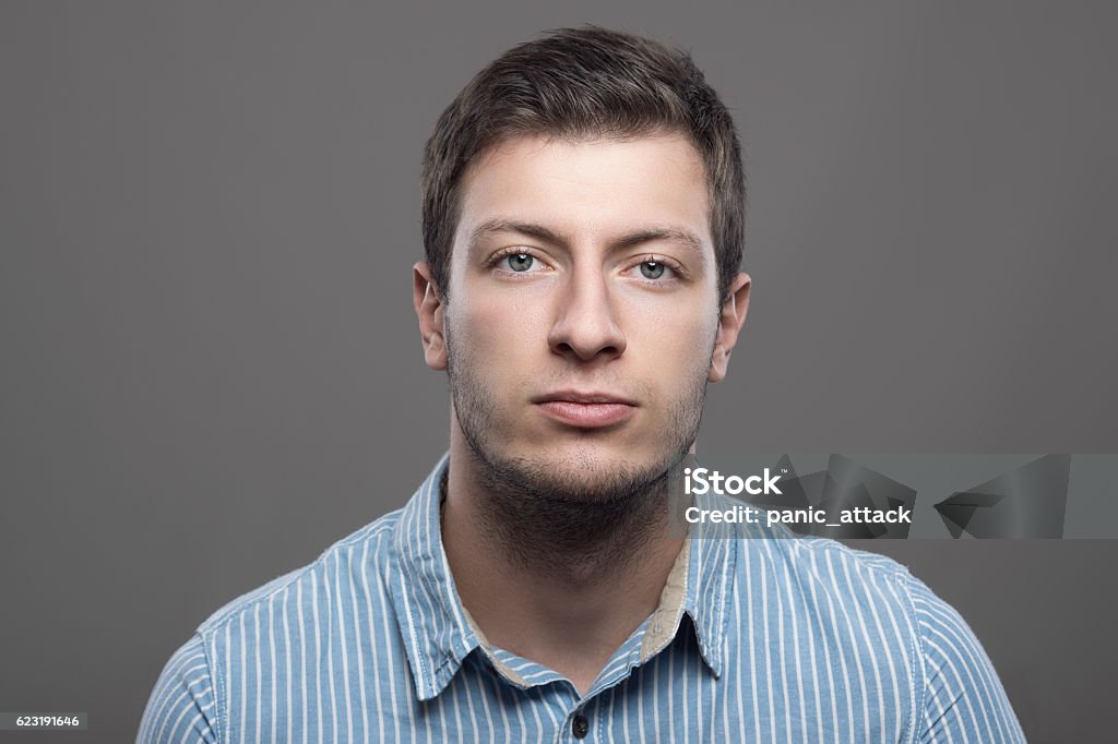 Young confident successful male ceo looking at camera Young confident successful male ceo in blue shirt looking at camera over gray background Serious Stock Photo