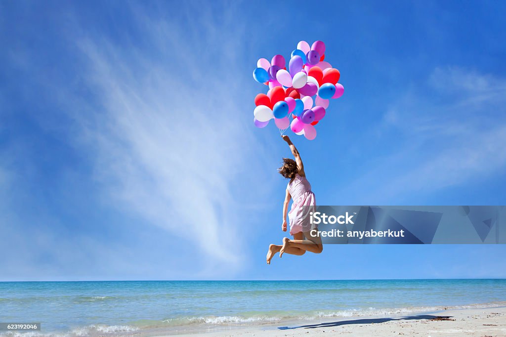 dream concept, girl flying with multicolored balloons, jump dream concept, girl flying on multicolored balloons in blue sky, imagination and creativity Women Stock Photo