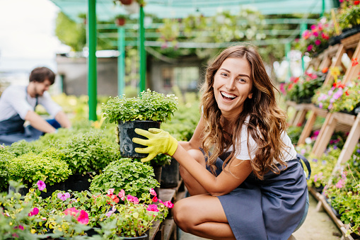 Smiling young woman holding potted flower in a greenhouse.