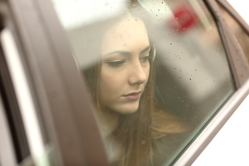 Closeup portrait of a worried car passenger looking at side through the window in a sad rainy day