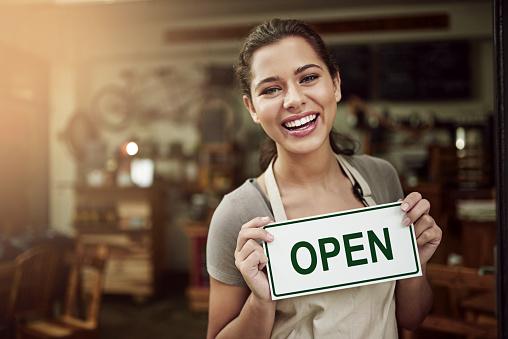 Portrait of a young woman holding up an open sign in her store