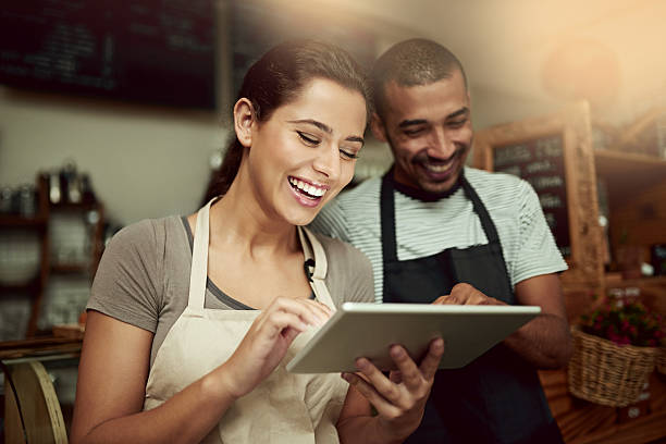 The smartest entrepreneurs use the smartest technologies Shot of a young man and woman using a digital tablet together while working in a coffee shop cafe tablet stock pictures, royalty-free photos & images