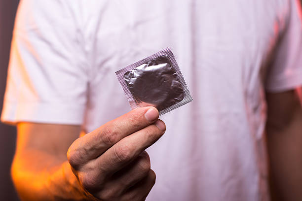 手にコンドームを持っている白いシャツを着た未知の男 - condom contraceptive sensuality healthcare and medicine ストックフォトと画像