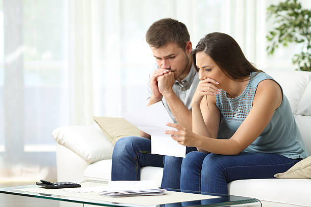 Worried couple reading a letter Worried couple reading an important notification in a letter sitting on a couch in the living room at home foreclosure photos stock pictures, royalty-free photos & images