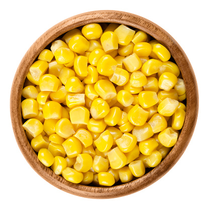 Sweet corn kernels in wooden bowl over white. Cooked canned yellow vegetable maize, Zea mays, also called sugar or pole corn, a vegetarian staple food. Isolated macro food photo close up from above.