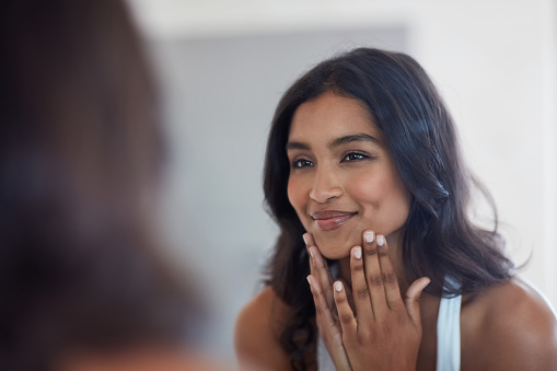 Shot of a beautiful young woman admiring herself in the mirror at home