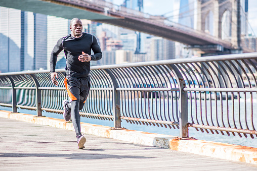 Young black man is exercising in New York, USA. He is running. River and city in the back.