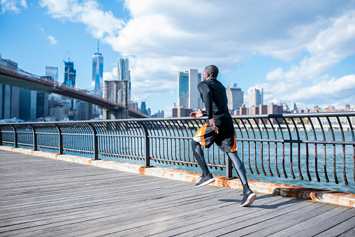 Young black man is exercising in New York, USA. He is running. River and city in the back.